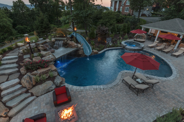 A luxurious pool at night with a vibrant fire pit party by the pool