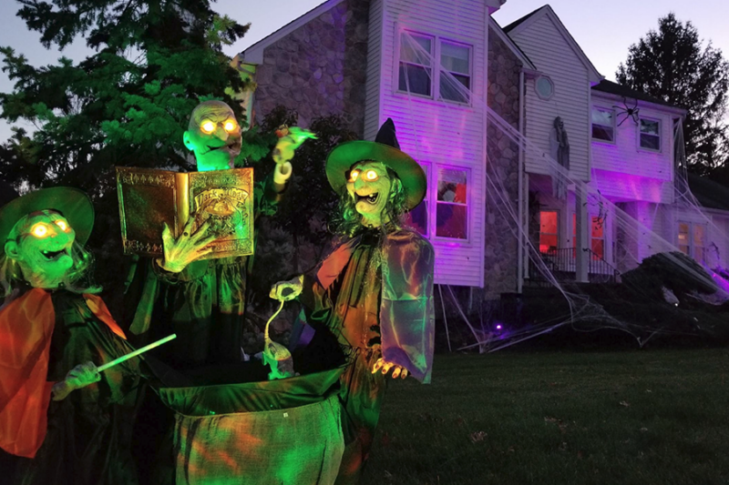 Three spooky witches casting their enchantments outside a haunted house, surrounded by eerie Halloween decorations.