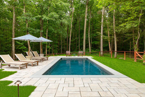 Inviting outdoor pool surrounded by pool umbrellas and chairs, nestled in lush greenery, exemplifying the excellence of NY pool cleaning services.