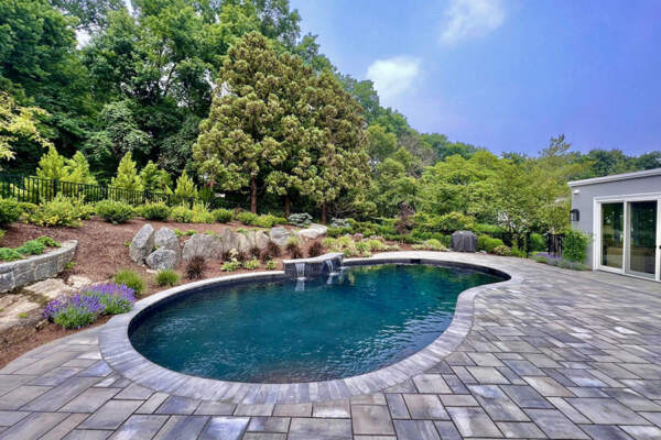 Simple serene pool with a waterfall water feature and natural scenery in the background, showcasing the quality of tri-state pool cleaning services.